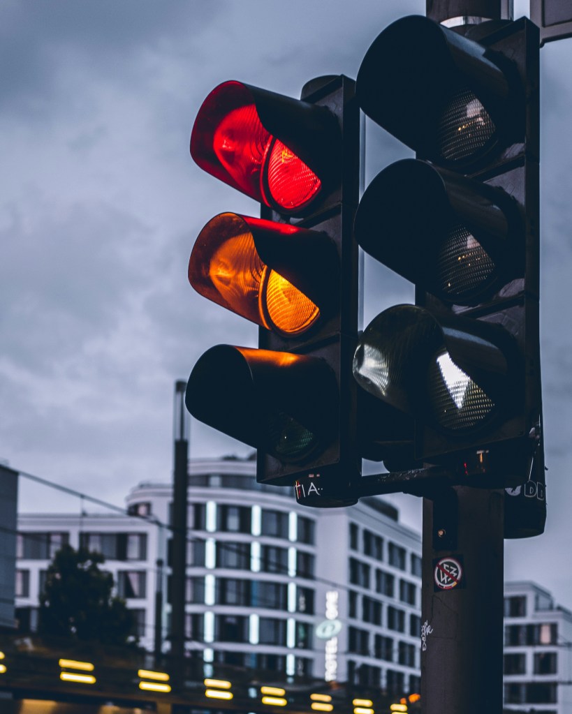 Traffic light displaying red and yellow lights against an urban backdrop, with cloudy skies.